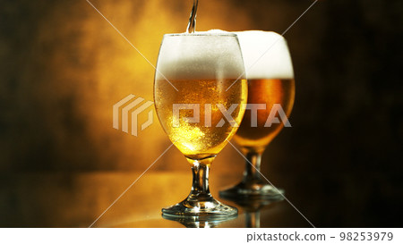 Glass of pouring light beer on dark golden background. Glass of pouring light beer on dark golden background. 98253979