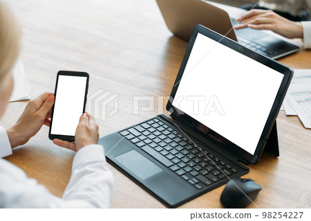 Digital mockup. Office woman. Computer technology. Female hands holding smartphone sitting desk with laptop blank screen in light room interior. 98254227