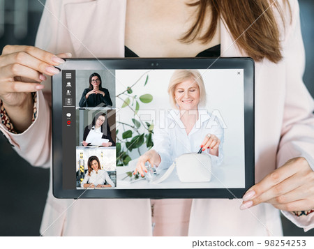 Video meeting. Digital briefing. Distant communication. Woman showing female successful business team chatting online on tablet screen. Video meeting. Digital briefing. Distant communication. Woman showing female successful business team chatting online on tablet screen. 98254253