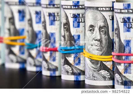 A row of rolled hundred dollar bills with rubber bands on dark background 98254822