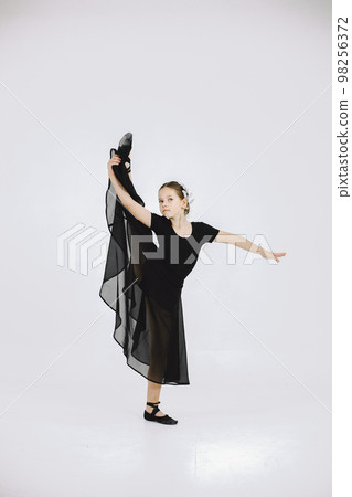 Little ballerina on white background. Brunette girl wearing black ballet suit. Girl doing gymnastic excercises. 98256372