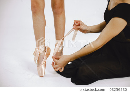 Focus on a legs in pointe shoes. Little ballerina on white background. Woman helping her daughter with a shoes. Focus on a legs in pointe shoes. Little ballerina on white background. Woman helping her daughter with a shoes. 98256380