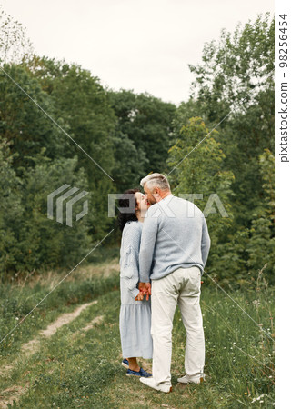 Close up romantic couple kissing in an autumn park. Man and woman wearing blue sweaters. Woman is brunette and man is gray. 98256454
