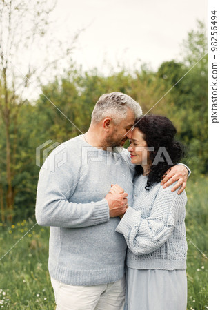Close up romantic couple standing in autumn park and hugging in daytime. Man and woman wearing blue sweaters. Woman is brunette and man is gray. Close up romantic couple standing in autumn park and hugging in daytime. Man and woman wearing blue sweaters. Woman is brunette and man is gray. 98256494
