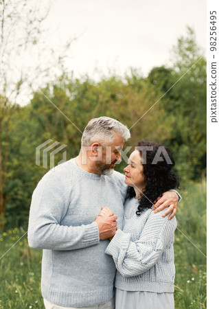Close up romantic couple standing in autumn park and hugging in daytime. Man and woman wearing blue sweaters. Woman is brunette and man is gray. 98256495