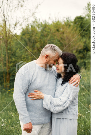Close up romantic couple standing in autumn park and hugging in daytime. Man and woman wearing blue sweaters. Woman is brunette and man is gray. Close up romantic couple standing in autumn park and hugging in daytime. Man and woman wearing blue sweaters. Woman is brunette and man is gray. 98256496