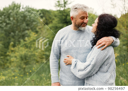 Close up romantic couple standing in autumn park and hugging in daytime. Man and woman wearing blue sweaters. Woman is brunette and man is gray. Close up romantic couple standing in autumn park and hugging in daytime. Man and woman wearing blue sweaters. Woman is brunette and man is gray. 98256497