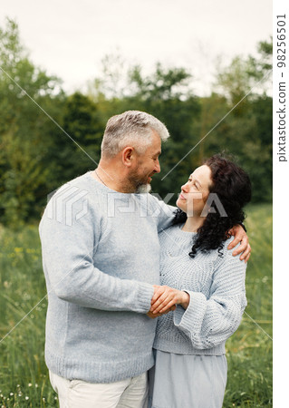 Close up romantic couple standing in autumn park and hugging in daytime. Man and woman wearing blue sweaters. Woman is brunette and man is gray. 98256501