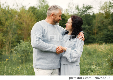 Close up romantic couple standing in autumn park and hugging in daytime. Man and woman wearing blue sweaters. Woman is brunette and man is gray. 98256502