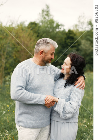 Close up romantic couple standing in autumn park and hugging in daytime. Man and woman wearing blue sweaters. Woman is brunette and man is gray. 98256503