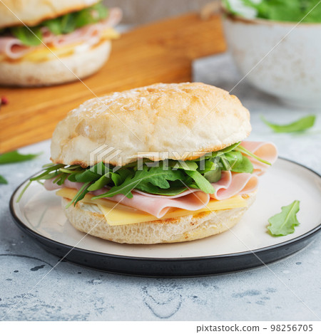 Two homemade sandwiches with ham, cheese and arugula on a concrete table. 98256705