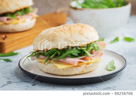 Two homemade sandwiches with ham, cheese and arugula on a concrete table. Two homemade sandwiches with ham, cheese and arugula on a concrete table. 98256706