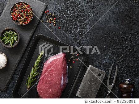 Raw beef fillet steak in vacuum tray with pepper on on black background with meat cleaver Raw beef fillet steak in vacuum tray with pepper on on black background with meat cleaver 98256891