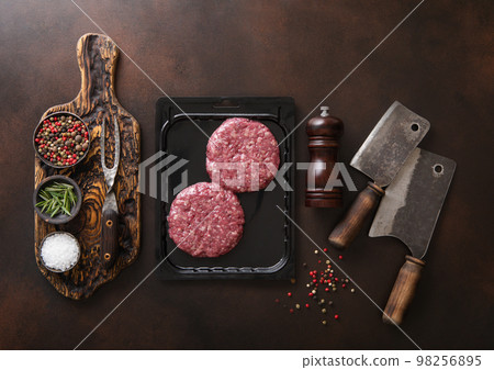 Raw beef burgers sealed in vacuum tray with cleavers on dark kitchen table with pepper grinde Raw beef burgers sealed in vacuum tray with cleavers on dark kitchen table with pepper grinde 98256895