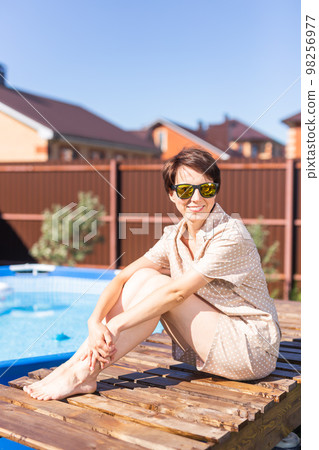 Portrait of pretty young woman in pajama sitting near inflatable swimming pool - summer and country life Portrait of pretty young woman in pajama sitting near inflatable swimming pool - summer and country life 98256977