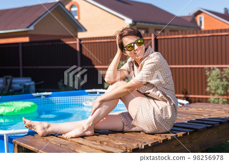 Portrait of pretty young woman in pajama sitting near inflatable swimming pool - summer and country life concept Portrait of pretty young woman in pajama sitting near inflatable swimming pool - summer and country life concept 98256978