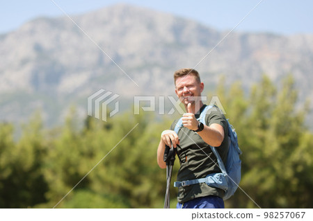 Happy hiker with backpack showing thumbs up against background of mountains on sunny day. Happy hiker with backpack showing thumbs up against background of mountains on sunny day. 98257067