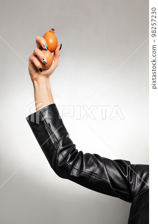 A woman's hand in a leather jacket, holding chicken eggs. Close up and copy space. Feminism, girl power, and the concept of equal rights and independence for women A woman's hand in a leather jacket, holding chicken eggs. Close up and copy space. Feminism, girl power, and the concept of equal rights and independence for women 98257230