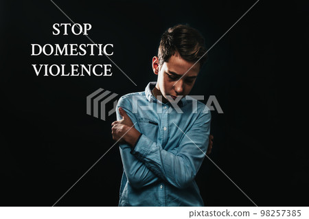 The concept of domestic violence. The sad teenage boy crossed his arms over his chest in defence of the attacks. Black backgroun. Text Stop domestic violence The concept of domestic violence. The sad teenage boy crossed his arms over his chest in defence of the attacks. Black backgroun. Text Stop domestic violence 98257385