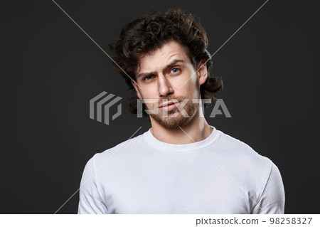 skeptic and nervous man in white t-shirt on dark gray background skeptic and nervous man in white t-shirt on dark gray background 98258327