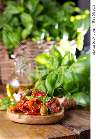 Dried tomatoes in olive oil and capers in piala, basil next to the product. Leaking oil. Traditional 98259918