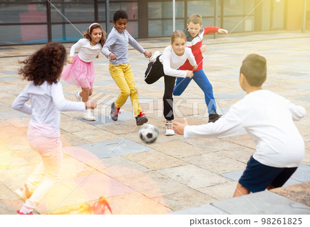 Cheerful tween schoolchildren playing with ball near school Cheerful tween schoolchildren playing with ball near school 98261825