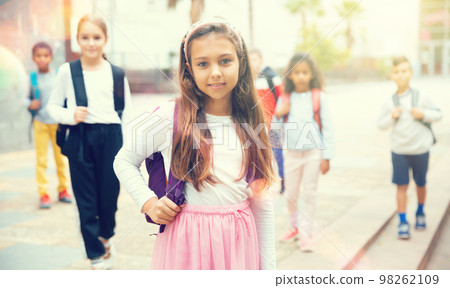 Positive schoolgirl standing near school, children on background Positive schoolgirl standing near school, children on background 98262109