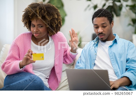 Annoyed black woman holding credit card, couple banking online Annoyed black woman holding credit card, couple banking online 98265067