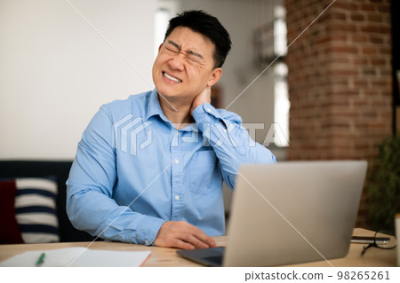 Neck ache. Mature asian man massaging aching neck, suffering from pain while working on laptop at table at home office Neck ache. Mature asian man massaging aching neck, suffering from pain while working on laptop at table at home office 98265261