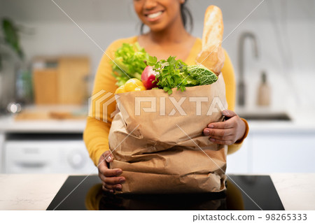 Smiling young african american female hold paper bag with groceries in modern kitchen interior 98265333