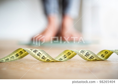 Feet of young african american woman on floor with selective focus on measuring tape in room interior Feet of young african american woman on floor with selective focus on measuring tape in room interior 98265404