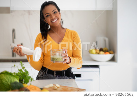 Happy young african american woman making smoothie with blender at table with organic vegetables 98265562