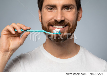Happy caucasian man cleaning teeth with toothbrush and smiling, standing over grey studio background 98265599