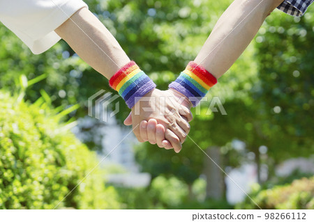 A male couple walking outdoors wearing rainbow colored wristbands Faceless 98266112