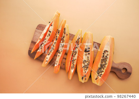 top view of slice of papaya on a chopping board on orange background  98267440