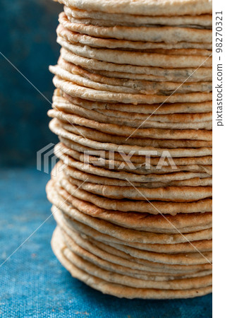 Flatbread lavash, chapati, naan, heap of tortilla on a blue background Homemade flatbread stacked. Flatbread lavash, chapati, naan, heap of tortilla on a blue background Homemade flatbread stacked. 98270321