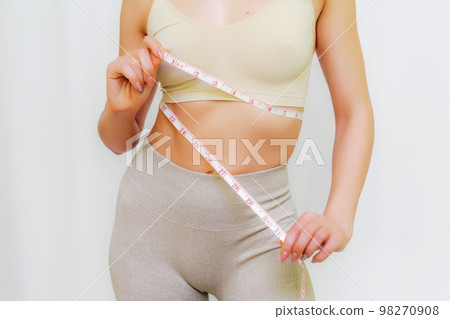 Close up of slim woman measuring her waist's size with tape measure. Isolated on white background. Close up of slim woman measuring her waist's size with tape measure. Isolated on white background. 98270908