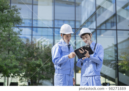 Two men in work clothes talking while looking at a tablet screen Construction management image 98271889