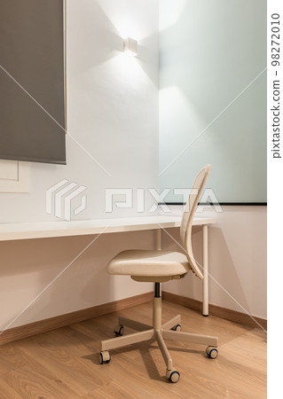 Close-up of work area with white table against wall with beige soft leather office chair for comfortable and productive work online on parquet floor. Room with bright artificial light. Close-up of work area with white table against wall with beige soft leather office chair for comfortable and productive work online on parquet floor. Room with bright artificial light. 98272010