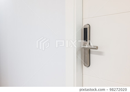 Closeup of an entrance white door with an electronic mortise lock. An electronic unit with display is built into metal handle. Opening doors with plastic card with microchip or digital code. Closeup of an entrance white door with an electronic mortise lock. An electronic unit with display is built into metal handle. Opening doors with plastic card with microchip or digital code. 98272020