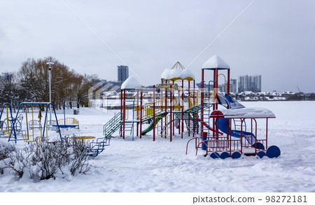 Children's colorful playground in the snow on the lake in the city park Children's colorful playground in the snow on the lake in the city park 98272181