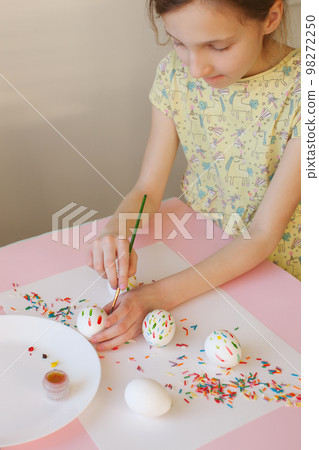 A ten-year-old girl decorates an egg for Easter. A ten-year-old girl decorates an egg for Easter. 98272250