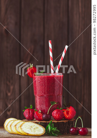 Side view of glass with fresh crimson smoothie with banana and berries on wooden table. Good food Side view of glass with fresh crimson smoothie with banana and berries on wooden table. Good food 98272995