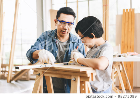 Southeast asian father teach using tools about carpenter skill with son at home workshop 98273089