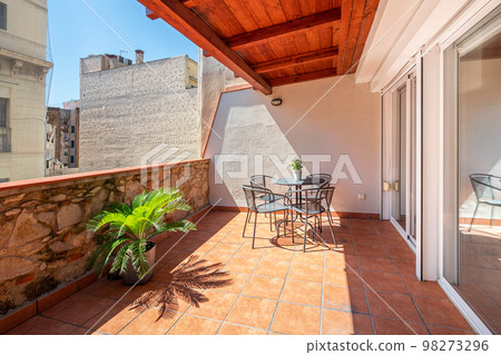 Spacious terrace under bright sunlight with warm pleasant exterior. In center is table for morning breakfast and lunch siesta. Roof protects from scorching sun and rain, floor is made of tiles. 98273296