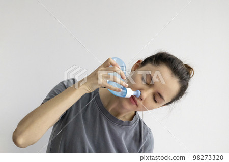 Girl rinses her nose with saline solution at home Using Neti Pot. Treatment and prevention of colds. How to rinse your nose when you have a runny nose. Girl rinses her nose with saline solution at home Using Neti Pot. Treatment and prevention of colds. How to rinse your nose when you have a runny nose. 98273320