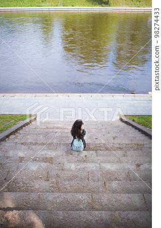 Beautiful girl sits and looks at the river Vilnius 98274433