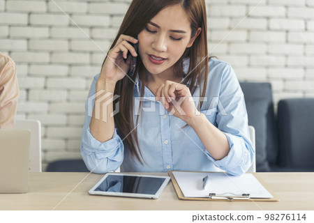 Asian women talk via smartphone work from home small office desk. Young asian Woman hands holding phone technology lifestyle. Happy Women person calling use digital smart phone working home office 98276114
