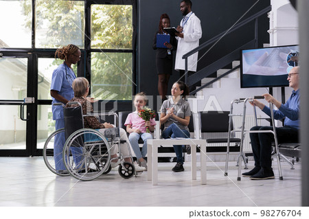Physician nurse discussing medical diagnosis with family explaining health care treatment during checkup visit in hospital reception. Elderly woman in wheelchair finising consultation 98276704