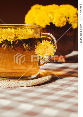 Dandelion flower healthy tea in glass cup on table. Herbal medicine Delicious tisane tea from with fresh yellow blossom dandelion flowers inside tea cup. Green clearing infusion Wildflowers Eco Dandelion flower healthy tea in glass cup on table. Herbal medicine Delicious tisane tea from with fresh yellow blossom dandelion flowers inside tea cup. Green clearing infusion Wildflowers Eco 98276861
